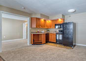 Thumbnail 6 of 33 - A kitchen with brown cabinets and a black fridge.