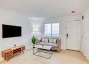Thumbnail 3 of 33 - A living room with a grey couch, a wooden coffee table, and a flat screen TV mounted on the wall.
