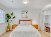 Thumbnail 4 of 33 - A bedroom with a large bed, a painting on the wall, and a potted plant on the side table.