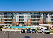 Thumbnail 31 of 40 - A large apartment complex with a pool and cars parked in the lot.