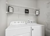 Thumbnail 3 of 56 - Two white washing machines in a laundry room with shelves above them.