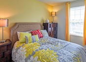 Thumbnail 20 of 36 - A bed with a grey and yellow comforter with a headboard and a nightstand with a lamp.