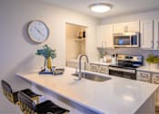 Thumbnail 2 of 20 - A kitchen with a white countertop and a clock on the wall.