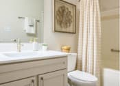Thumbnail 8 of 20 - A white toilet sits in a bathroom with a white sink and a shower curtain.