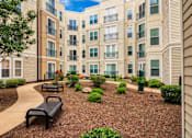 Thumbnail 1 of 62 - A black bench sits in the middle of a landscaped courtyard.