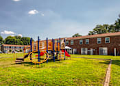 Thumbnail 5 of 26 - A playground with a swing set and a red slide in the foreground and apartment buildings in the background.