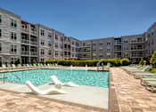 Thumbnail 11 of 35 - A large swimming pool surrounded by lounge chairs and apartment buildings.