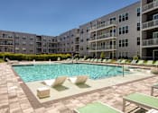 Thumbnail 10 of 35 - A large outdoor swimming pool surrounded by lounge chairs and buildings.