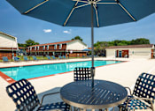 Thumbnail 1 of 26 - A table with chairs and an umbrella is in front of a pool.