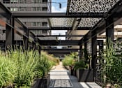 Thumbnail 27 of 55 - A walkway with a metal roof and concrete planters on either side.