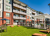 Thumbnail 35 of 40 - A sunny day at a modern apartment complex with a green lawn and picnic tables.