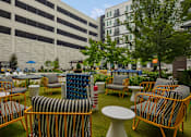 Thumbnail 5 of 40 - A patio with chairs and tables is surrounded by buildings.