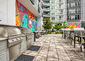Thumbnail 13 of 40 - A patio with a grill and chairs is surrounded by a colorful mural.