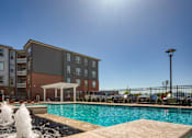 Thumbnail 37 of 40 - A sunny day at a pool with a fountain in the foreground and apartment buildings in the background.