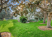 Thumbnail 1 of 13 - A house is surrounded by a green lawn and trees.
