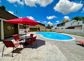 Thumbnail 5 of 16 - A pool area with a table and chairs and a red umbrella.