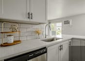 Thumbnail 8 of 13 - A kitchen with a black dishwasher and white cabinets.