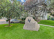Thumbnail 4 of 13 - A sign for Deer Creek Apartments is in the foreground of a grassy area.