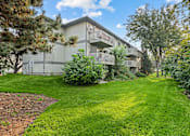 Thumbnail 3 of 13 - A grassy area in front of a building with trees and bushes.