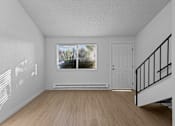 Thumbnail 10 of 15 - A room with a wooden floor, a window with blinds, a white door, and a staircase with a black railing.