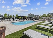 Thumbnail 3 of 25 - A pool area with sun loungers and a building in the background.
