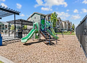 Thumbnail 5 of 25 - A playground with a green slide and a brown ground.