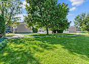 Thumbnail 30 of 34 - A large grassy area with trees and buildings in the background.