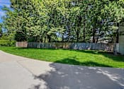 Thumbnail 29 of 34 - A concrete pathway leads through a grassy area with a fence and trees in the background.
