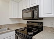 Thumbnail 12 of 34 - A black microwave is mounted above a black stove in a kitchen with white cabinets.