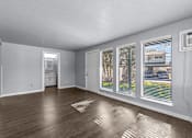 Thumbnail 1 of 34 - A room with wooden floors and white walls, with a window showing a view of a building outside.