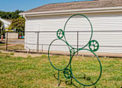 Thumbnail 48 of 61 - A green metal sculpture of a dog and paw prints sits in the grass in front of a white building.