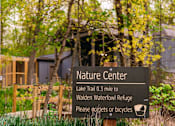 Thumbnail 54 of 61 - A nature center sign is in front of a building and trees.
