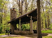 Thumbnail 57 of 61 - A small stone building with a chimney is surrounded by trees.