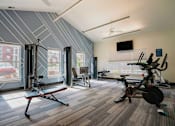 Thumbnail 9 of 36 - A home gym with a variety of equipment including a rowing machine, a bench press, and a stationary bike.