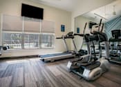 Thumbnail 12 of 36 - A gym with treadmills, elliptical machines, and a flat screen TV.