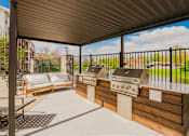 Thumbnail 18 of 36 - A patio with a grill and a couch under a roof.