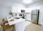 Thumbnail 22 of 36 - A kitchen with white cabinets and a white island.