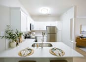 Thumbnail 24 of 36 - A kitchen with a white counter top and a stainless steel refrigerator.