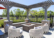 Thumbnail 3 of 21 - A patio with a fire pit and chairs under a pergola.