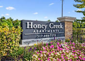 Thumbnail 2 of 42 - A sign for Honey Creek Apartments is surrounded by flowers.