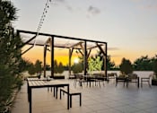 Thumbnail 7 of 17 - A sunset view of a patio with tables and chairs.