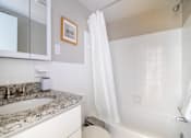 Thumbnail 15 of 16 - A white bathroom with a stone countertop and a white bathtub.