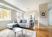 Thumbnail 6 of 16 - A grey couch with a throw is in a room with a wooden floor and a large window.