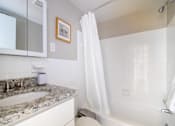 Thumbnail 16 of 18 - A white bathroom with a marble counter top and a white tub.