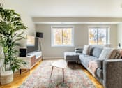 Thumbnail 5 of 18 - A living room with a grey couch, a television, and a plant.