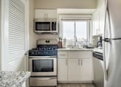 Thumbnail 10 of 18 - A kitchen with a stove, oven, refrigerator, microwave, and cabinets.
