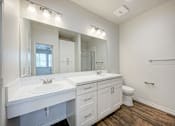 Thumbnail 12 of 18 - A white bathroom with a double sink and a toilet.