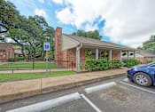 Thumbnail 13 of 18 - A blue car is parked in a parking space next to a building with a covered porch.