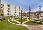 Thumbnail 7 of 14 - A playground with a slide, swings, and a seesaw in front of a building.