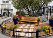 Thumbnail 4 of 14 - A small park with a bench, a tree, and flower pots.